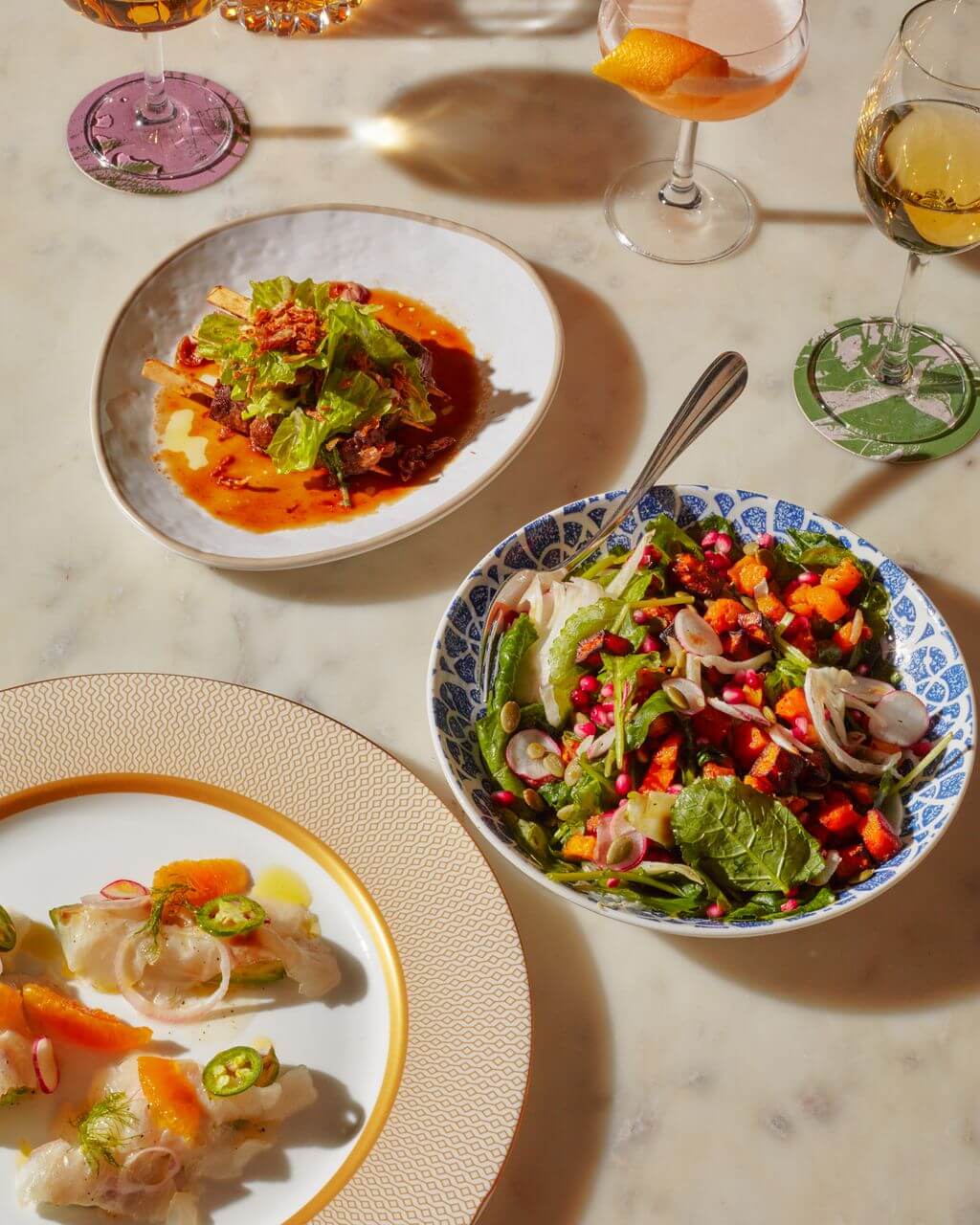 A table setting with three plates of food and two wine glasses
