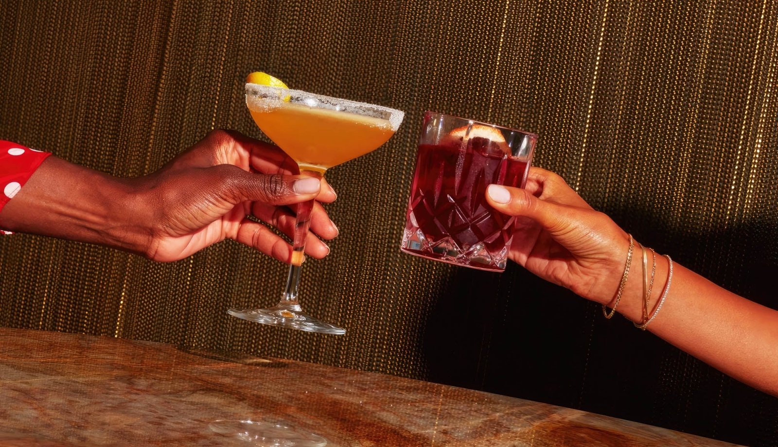 Two women clinking two cocktails together.