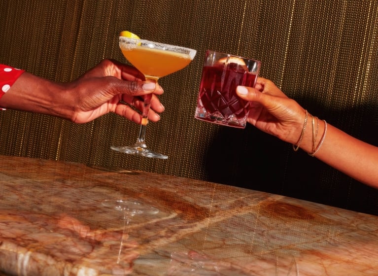 Two women clinking two cocktails together.