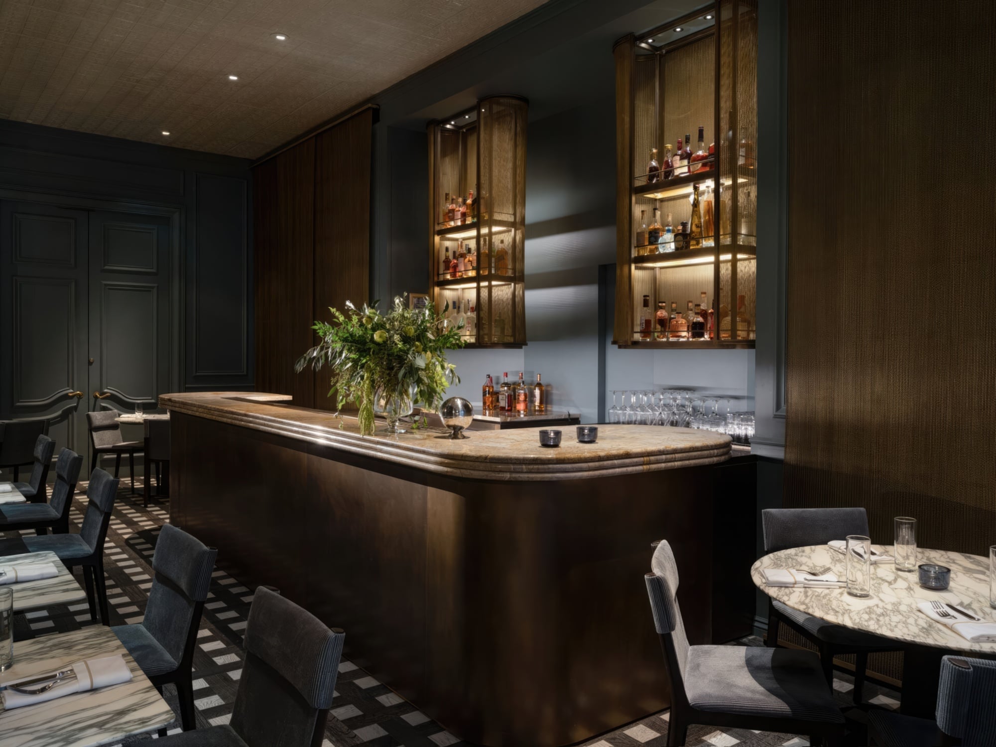 a dimly lit bar with a curved marble countertop and glass shelves filled with bottles