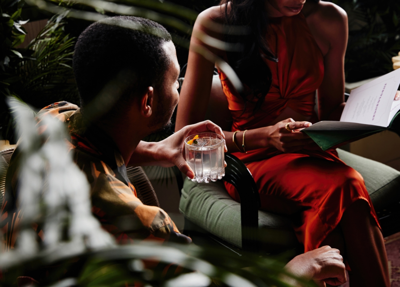 A couple reading a restaurant menu while drinking cocktails.