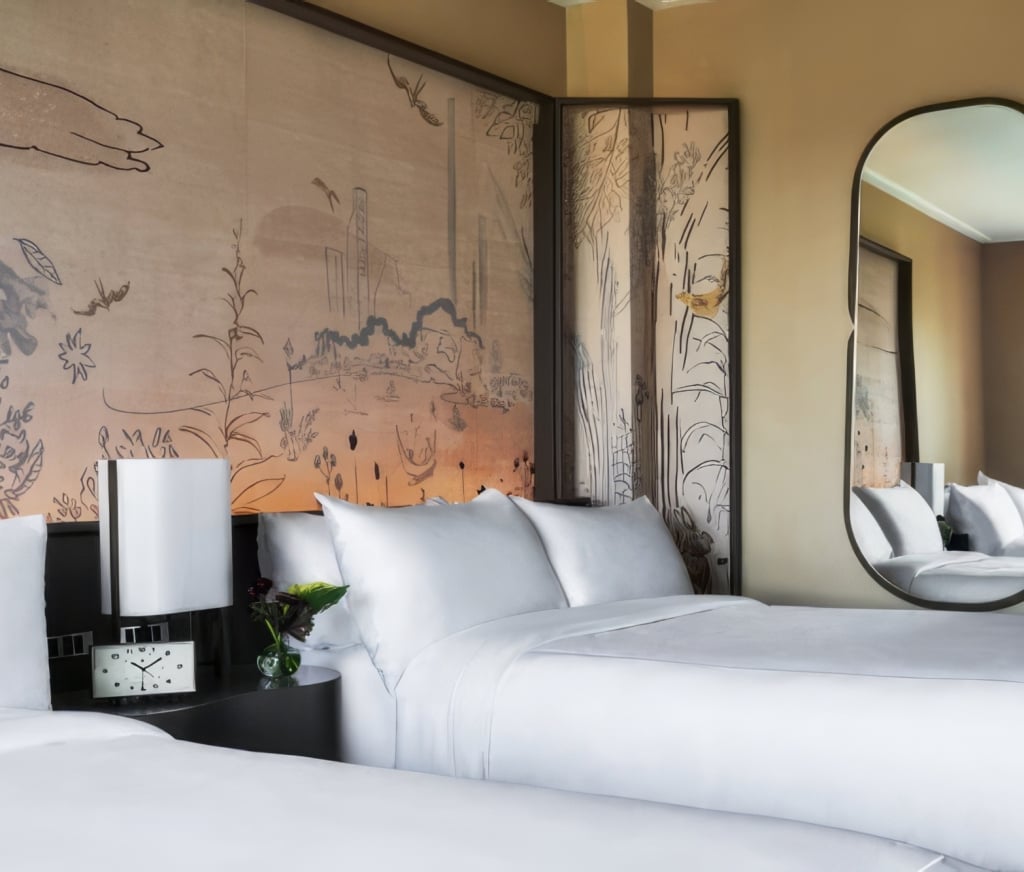 A hotel room with a large bed, white bedding, and a decorative wall mural.
