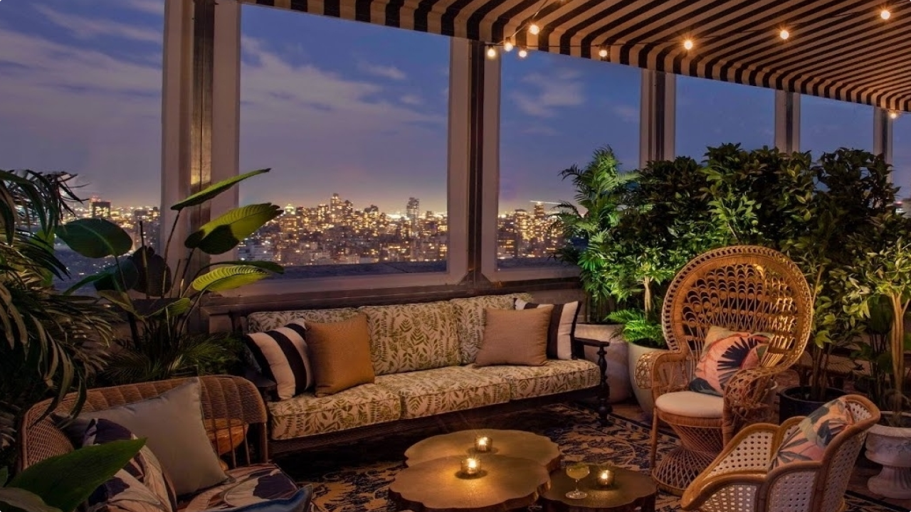 A lounge area with a sofa, coffee tables, and plants, offering a city view at dusk.