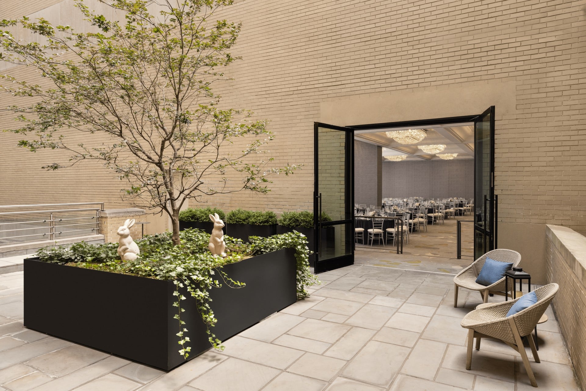 A small outdoor seating area with planters, a tree, and a glass door leading to a dining room.