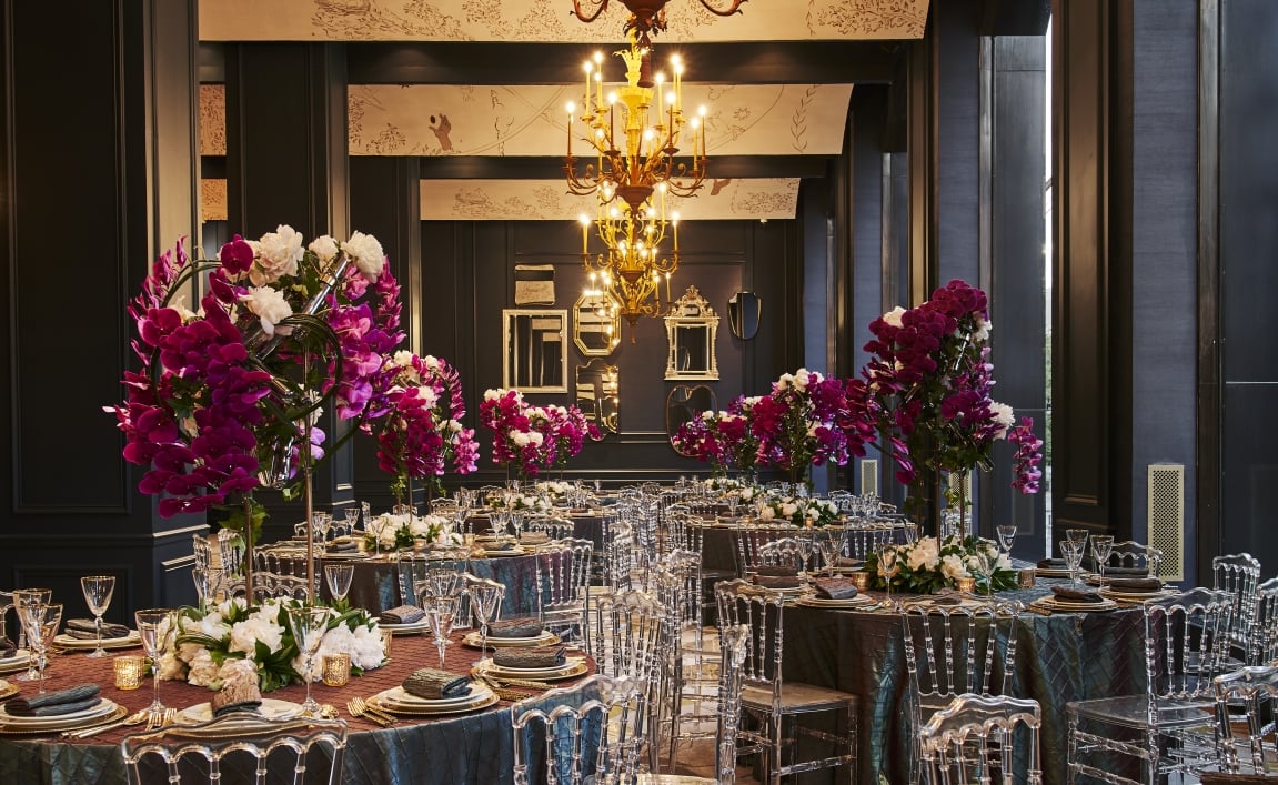 A formal dining room with tables set for a meal, decorated with flowers and a chandelier.