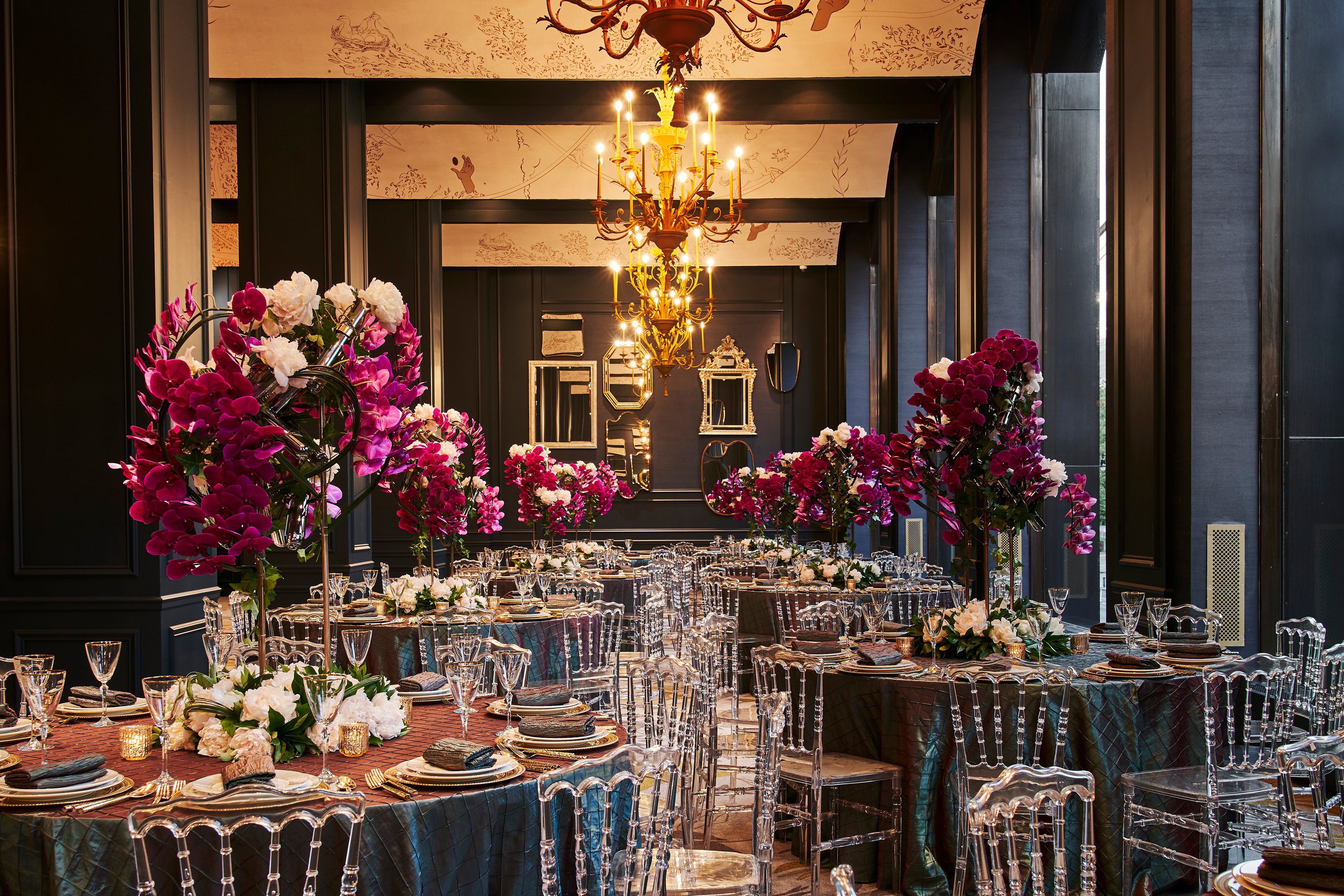 A formal dining room with tables set for a meal, decorated with flowers and a chandelier.