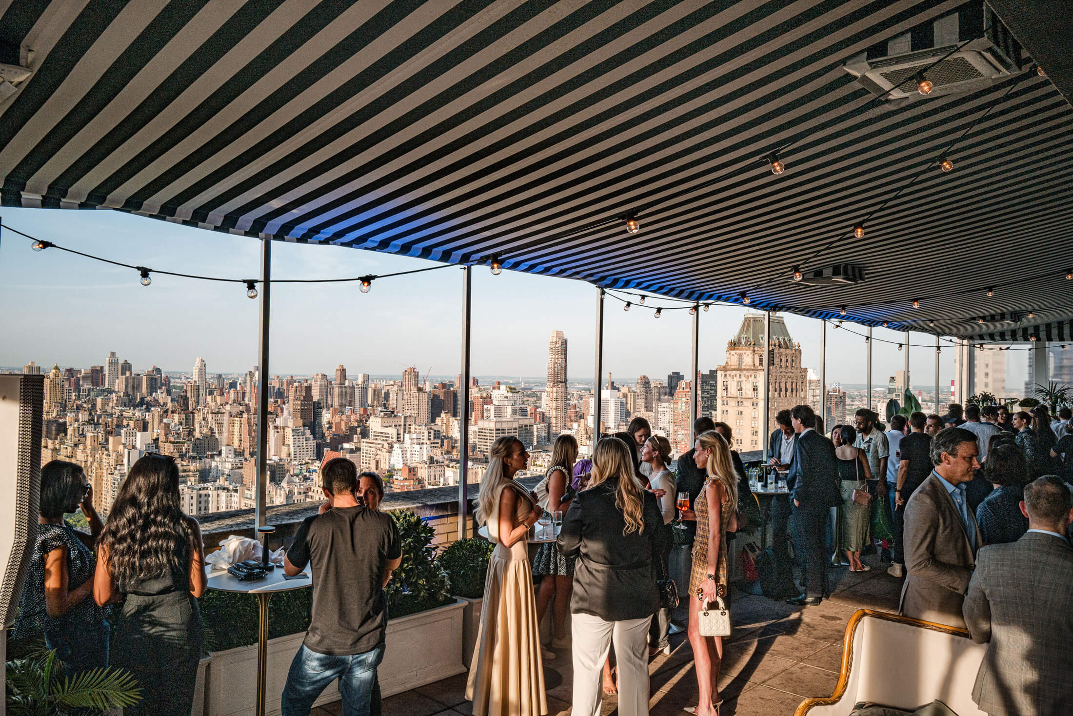 A group of people socializing at a rooftop bar with a city skyline view.