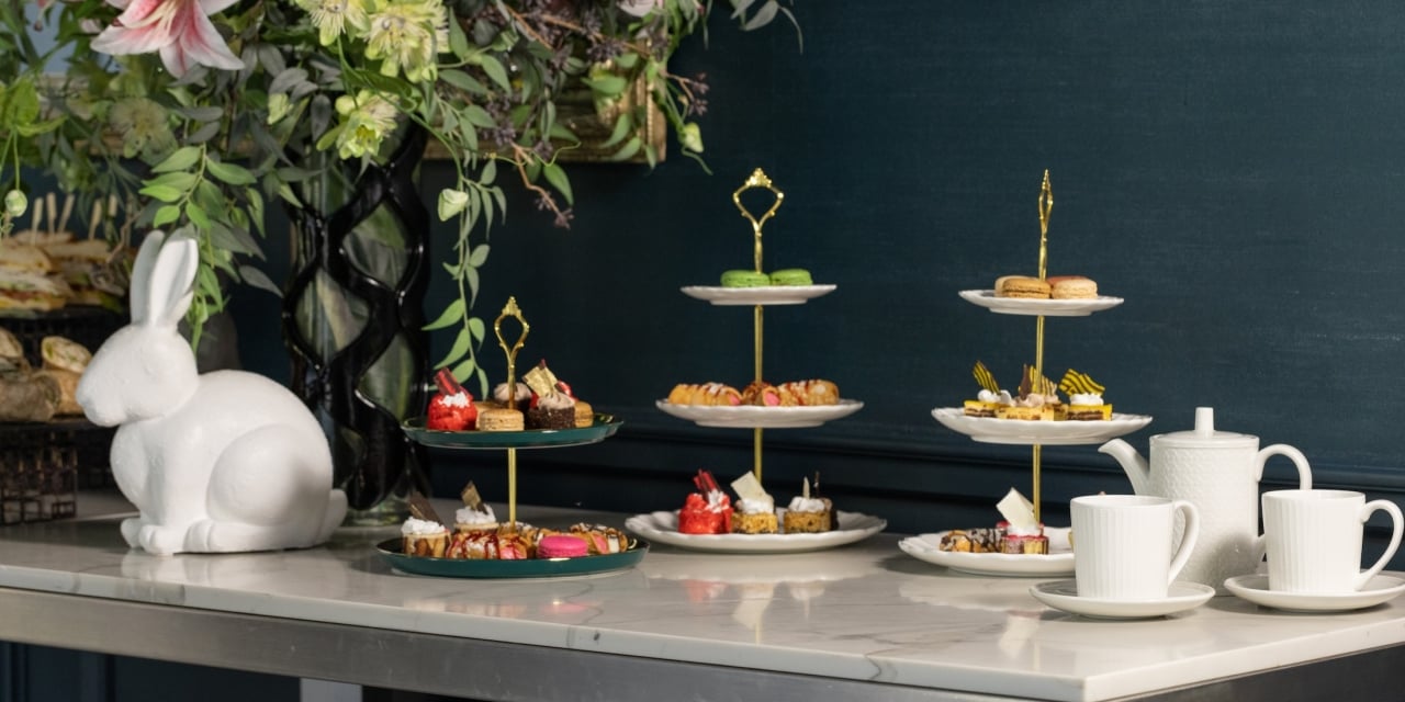 A table with pastries and tea on a white marble countertop with a white bunny statue and flowers in the background.