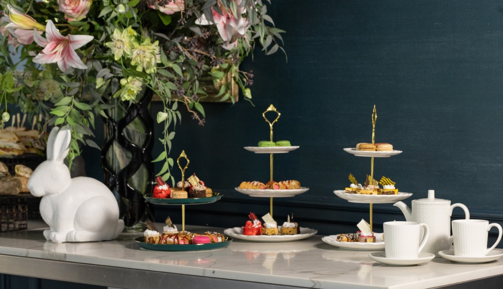 Three tiered trays of desserts on a table with a large bouquet of flowers.