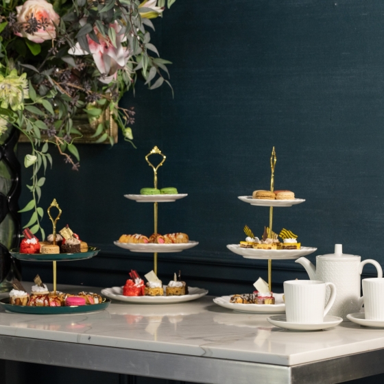 Three tiered trays of desserts on a table with a large bouquet of flowers.