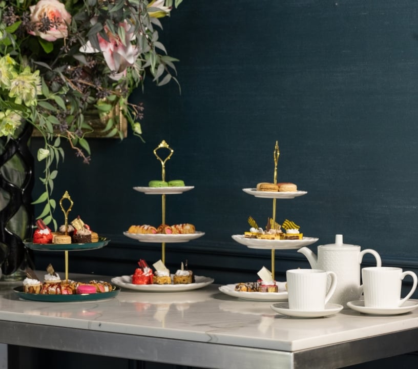 Three tiered trays of desserts on a table with a large bouquet of flowers.