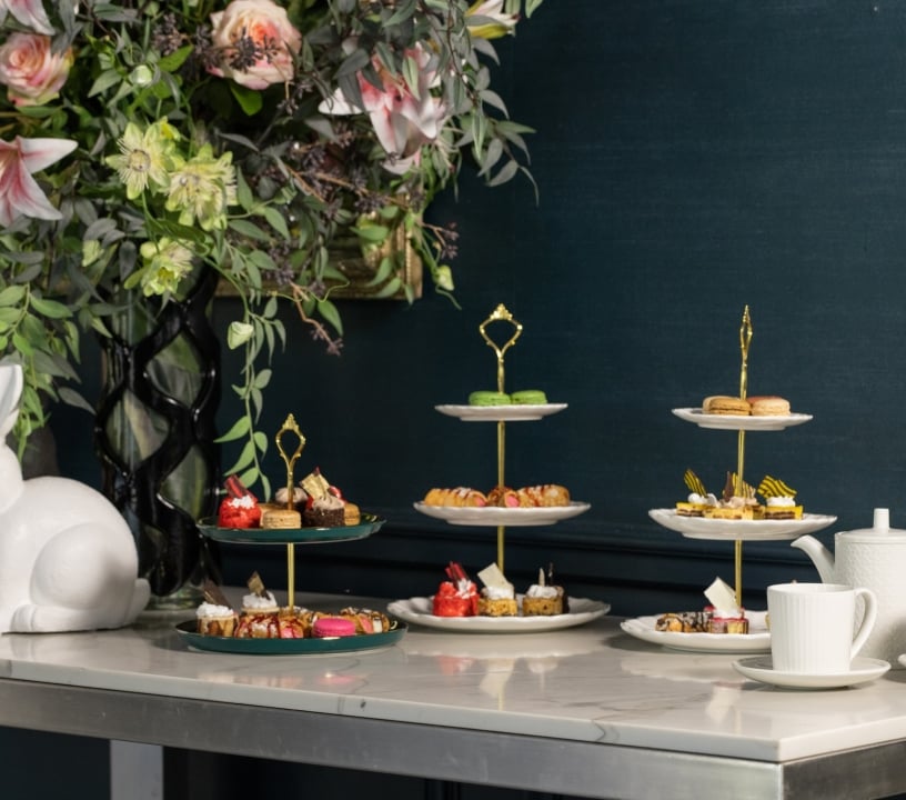 Three tiered trays of desserts on a table with a large bouquet of flowers.