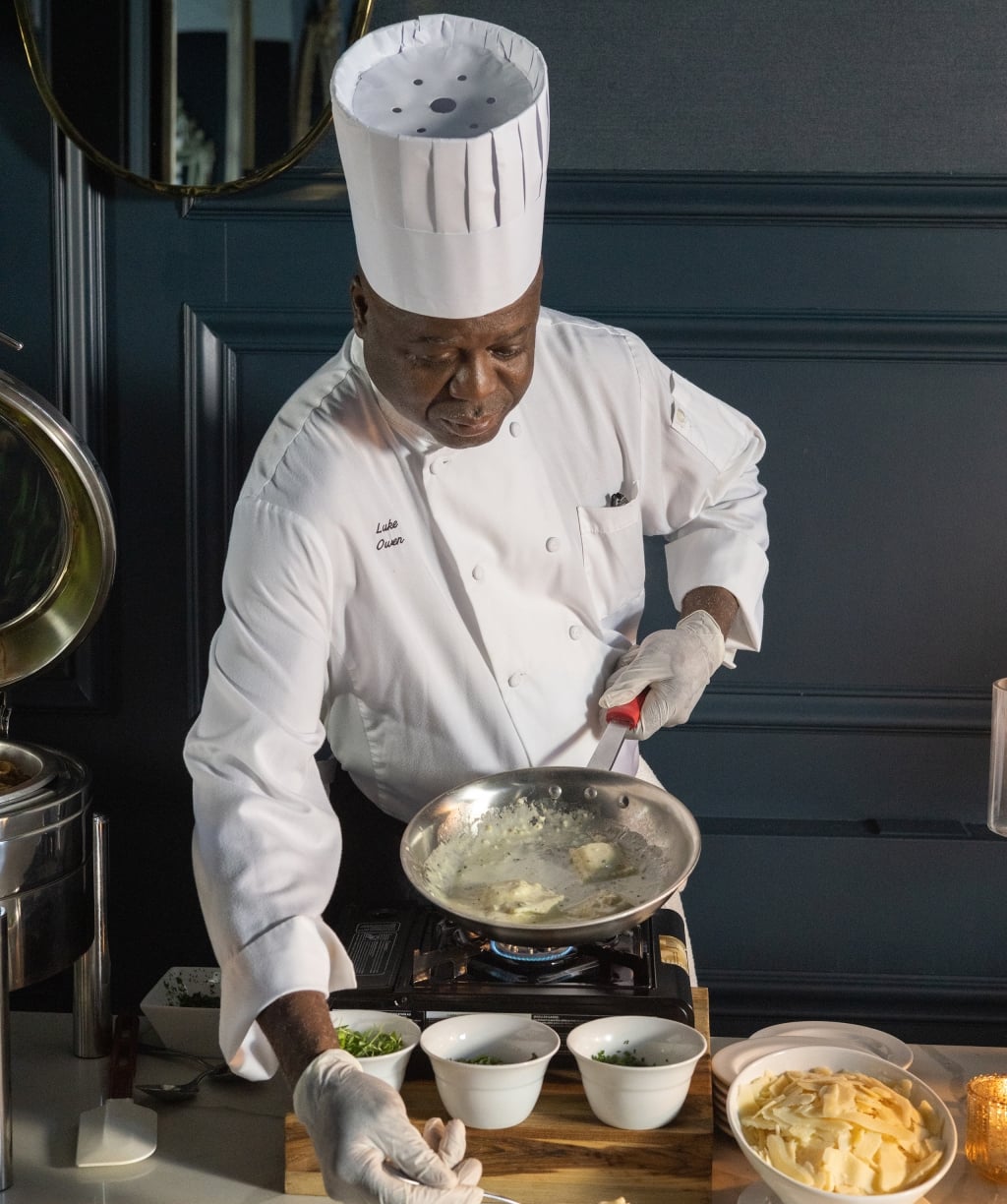 A chef in a white uniform cooking on a stovetop with various ingredients.