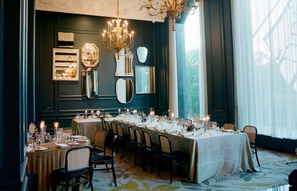A formal dining room with a long table, multiple chairs, a chandelier, and mirrors on the wall.