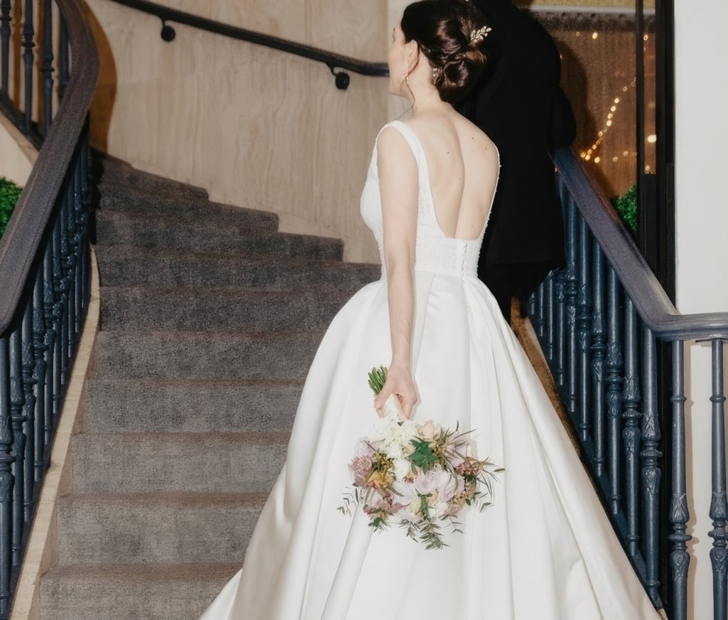 a woman in a wedding dress holding flowers walking up a staircase
