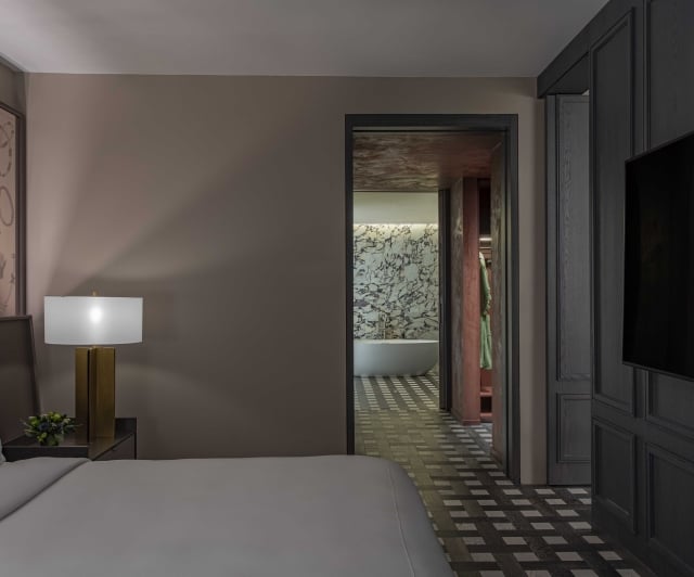 A hotel room with a bed, lamp, TV, and doorway to bathroom