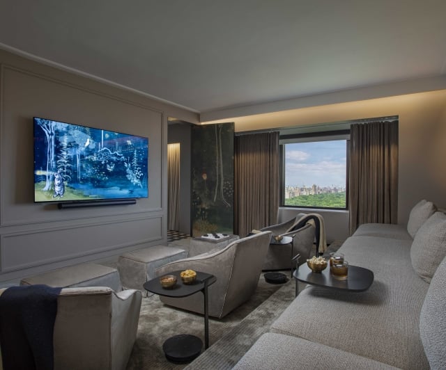 A wide living room with a large television, comfortable seating, and a city view.