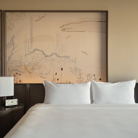 A king bed with side table and painted mural behind.