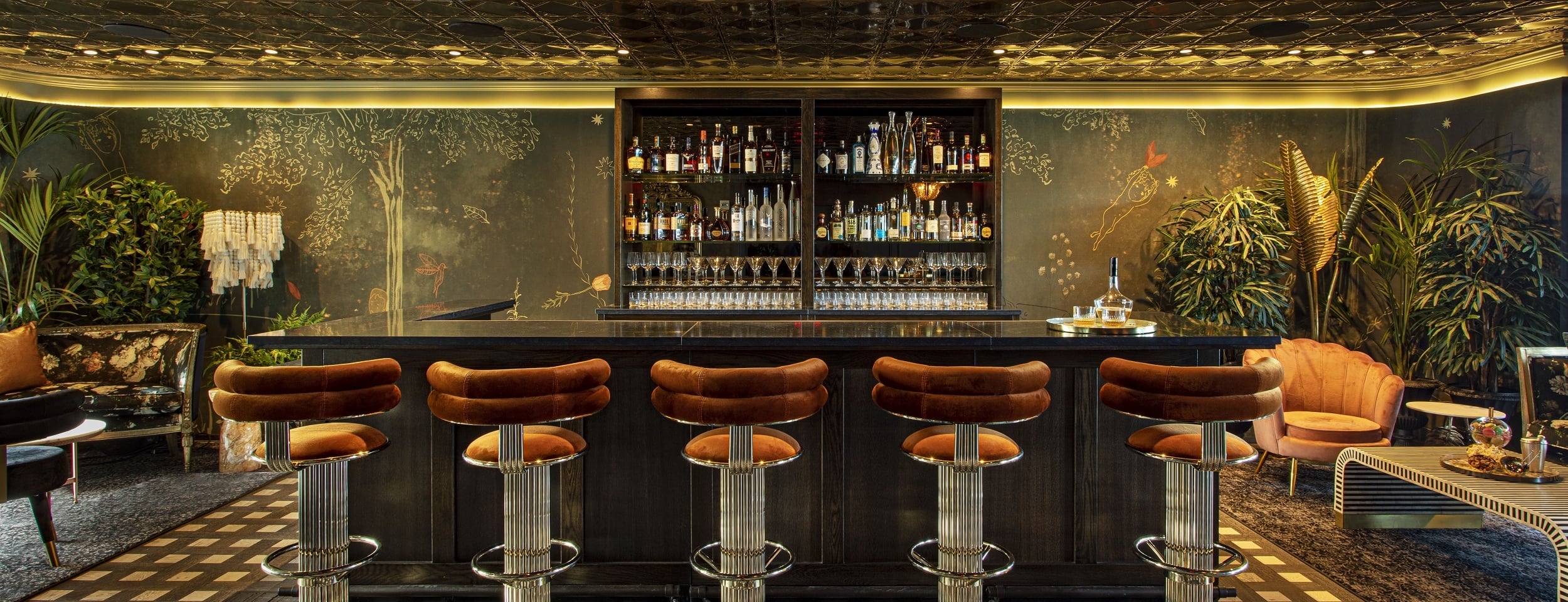 A luxurious bar with stools, a counter, and shelves stocked with bottles and glasses.